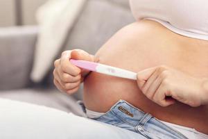 Happy pregnant woman resting on sofa with pregnancy test photo