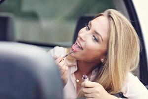 Young attractive woman looking in rear view mirror applying lipstick photo