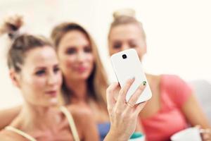 Three beautiful young women chilling at home and taking selfie photo