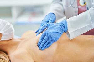 Doctor in mask checking up breast to her patient photo