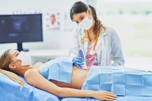 médico con máscara haciendo una prueba de ultrasonido en el abdomen a una paciente foto