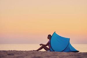 Silhouette of young woman in front of a tent at the beach at sunrise photo