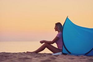 Silhouette of young woman in front of a tent at the beach at sunrise photo