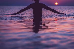 Silhouette of young woman practicing yoga on the beach at sunrise photo