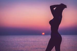 silueta de mujer sexy posando al amanecer en la playa foto