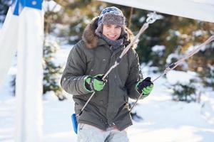 Young handsome man having fun on swing in winter scenery photo