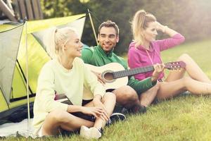 Group of friends camping in forest and playing guitar photo