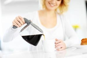 mujer joven sirviendo café en la cocina foto