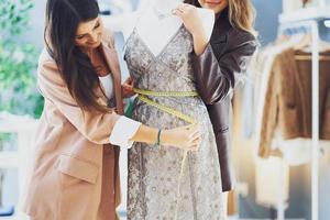 Two women tailors trying dress on mannequin photo