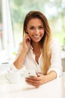 Young woman with coffee and smartphone in kitchen photo