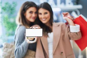 Two happy girls on shopping holding phone photo