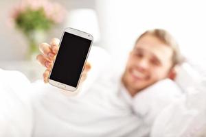 Handsome man lying in bed with smartphone photo