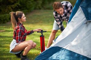 Una pareja joven y agradable divirtiéndose en acampar montando carpa foto