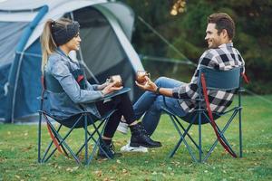 Young nice couple sitting on chairs inf front of tent on camping photo