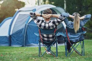 Young nice couple sitting on chairs inf front of tent on camping photo