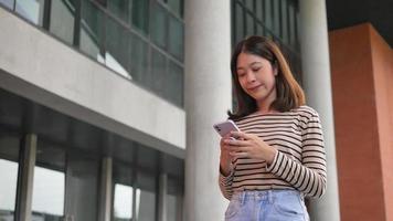 Frau mit digitalem Smartphone, die in sozialen Medien surft, posiert glücklich draußen und sendet mobile SMS, während Netzwerkseiten in den Straßen der Stadt stehen. video