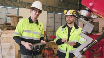 dos ingenieros de producción varones caucásicos prueban y controlan un brazo robótico en una fábrica de fabricación mecánica, máquinas automáticas inteligentes en negocios industriales e innovación tecnológica futurista. video