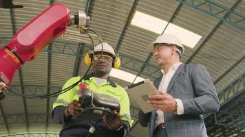 An African American engineer demonstrates smart robotic arm control to customer in mechanical manufacturing factory, intelligent automatic machines in industrial business, and futuristic technology. video