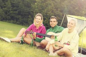 Group of friends camping in forest and playing guitar photo