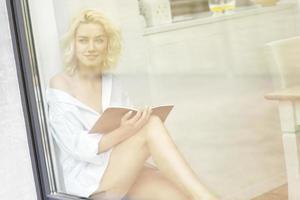 mujer bonita joven leyendo un libro en la ventana foto