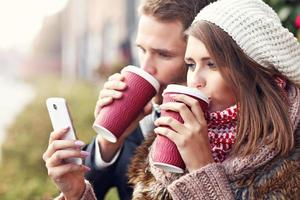 pareja joven sentada en un banco con café y teléfono inteligente foto