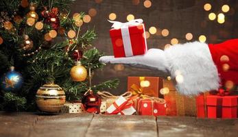 mano de santa claus sosteniendo un regalo de navidad envuelto. foto
