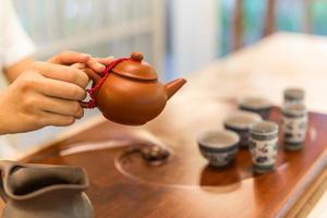 Tea is poured into the cup closeup. Asian tea set-up on wooden bamboo table, hand gently pouring Chinese tea photo