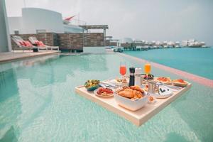 Breakfast in swimming pool, floating breakfast in luxurious tropical resort. Table relaxing on calm pool water, healthy breakfast and fruit plate by resort pool. Tropical couple beach luxury lifestyle photo