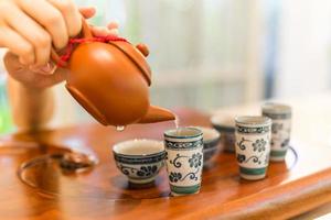 Tea is poured into the cup closeup. Asian tea set-up on wooden bamboo table, hand gently pouring Chinese tea photo