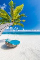 Tropical beach background as summer landscape with beach swing or hammock and white sand and calm sea for beach banner. Perfect beach scene vacation and summer holiday concept. Boost up color process photo