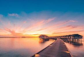 puesta de sol en la isla de maldivas. resort de bungalows de agua en la playa de las islas. océano índico, maldivas. hermoso paisaje de puesta de sol, resort de lujo y cielo colorido. puesta de sol de playa artística bajo un cielo maravilloso foto