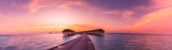 Amazing sunset panorama at Maldives. Luxury resort villas seascape with soft led lights under colorful sky. Maldives sunset seascape view. Horizon with sea and colorful sky. Wonderful sunset scenery photo