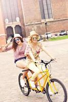 Two happy girl friends riding tandem bicycle photo