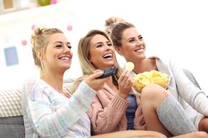 Three beautiful young women watching tv at home photo