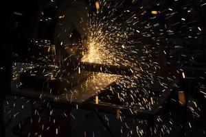 Lots of sparks from cutting metal in dark. Lights fly in different directions. Industrial background. photo