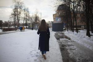 Girl walks down street in winter. Woman in winter in city. Bad road in yard in Russia. photo