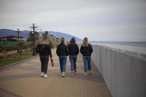 Young girls walk along the arranged promenade by the sea. Friends walk along the stone promenade. Shooting teenagers from the back. photo