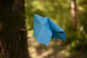 Paper airplane hangs on string. Origami made of blue paper. Decoration of park. photo