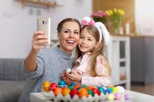 Mother and daughter painting Easter eggs and taking selfie photo