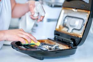 Woman cleaning grill or toaster machine in the kitchen