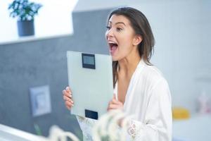 Young nice brunette woman in the bathroom with weight scale photo