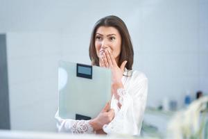 Young nice brunette woman in the bathroom with weight scale photo