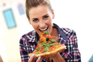 Beautiful young woman eating pizza at home photo