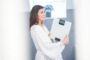 Young nice brunette woman in the bathroom with weight scale photo