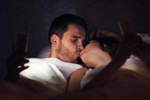 pareja joven usando teléfonos inteligentes en la cama por la noche foto