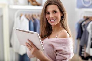 Happy woman in clothes shop holding tablet photo