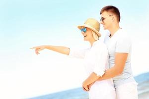 feliz pareja abrazándose en la playa y señalando foto