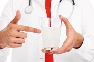 Midsection of a doctor holding glass of water with pill photo