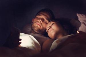 Young couple using smartphones in bed at night photo