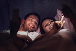 pareja joven usando teléfonos inteligentes en la cama por la noche foto